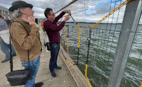 Stephen Huntley/BBC Campaigners chaining the word "unlock" to the fencing