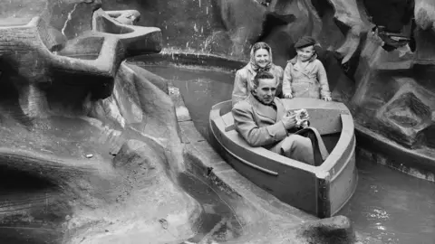 Historic England/John Laing Collection Two adults and a child ride water boat ride