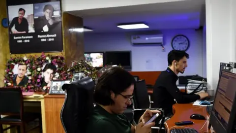 AFP Tolo News staff work on, with a memorial to lost colleagues in the background
