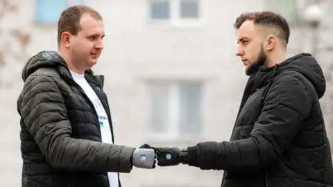 Superhumans Andrii (left) and Vitalii touching hands with their prosthetics