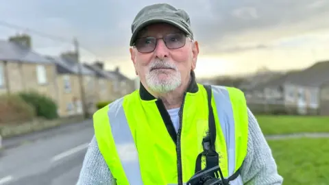 BBC Close up of a man in a cap and high vis jacket