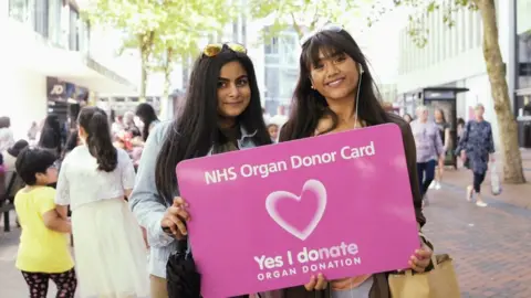 NHS Blood and Transplant Two Asian women holding up a sign that encourages people to become organ donors