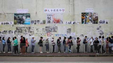 Getty Images People queue to cast their vote in front of a "Lennon Wall" adorned with tattered posters