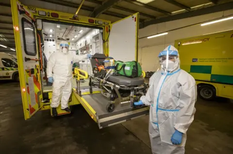 PA Media Paramedics wearing protective equipment remove a trolley bed from an ambulance