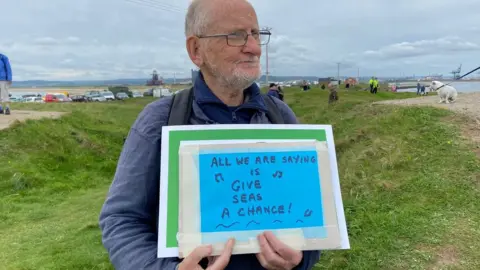 Man holds sign saying "all we are saying is give seas a chance"