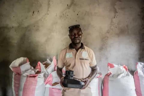 Moses Sawasawa/BBC Koko Bikuba, 37-year-old former combatant, holds a refractometer to measure the temperature of the coffee.