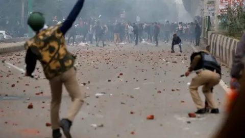 Reuters A riot police officer throws a piece of brick towards demonstrators during a protest against a new citizenship law in Seelampur, Delhi