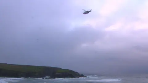 BBC The UK Coastguard search and rescue helicopter from Newquay flies over the coast