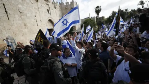 EPA Israeli nationalists wave flags and make obscene gestures towards Palestinian and foreign journalists outside Damascus Gate, an entrance to Jerusalem's Old City (18 May 2023)