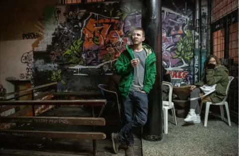 Chris Leslie A young man stands in the smoking area of a nightclub