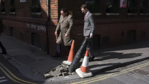 Getty Images Men walking past a damaged pavement