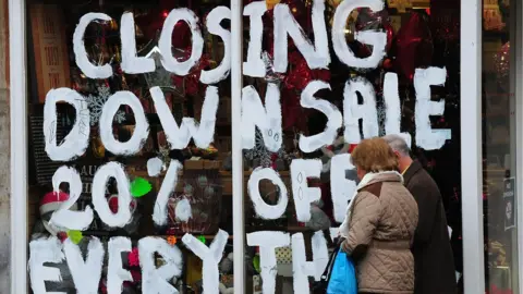 PA Media People walk past a store with the words 'Closing down sale 20% off everything' painted on the window