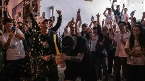 Getty Images A pro-democracy supporter opens a bottle of champagne outside a polling station to celebrate after pro-Beijing candidate Junius Ho lost a seat