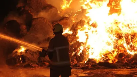 A firefighter attending a fire of hay bales