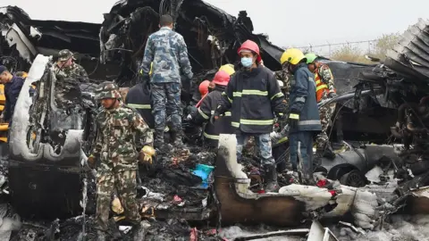 Getty Images Nepali rescue workers remove a body found in the wreckage of an airplane that crashed near the international airport in Kathmandu on March 12, 2018. Forty-nine people were killed when a Bangladeshi plane crashed and burst into flames near Kathmandu airport on March 12, in the worst aviation disaster to hit Nepal in nearly three decades.