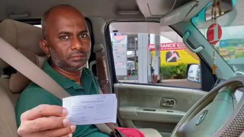 Mr Sadasivam holds up his token reserving his place in line