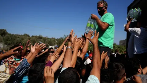 EPA Migrants receive food, fruit and water near the sit of the Moria camp on the island of Lesbos, Greece, 10 September 2020