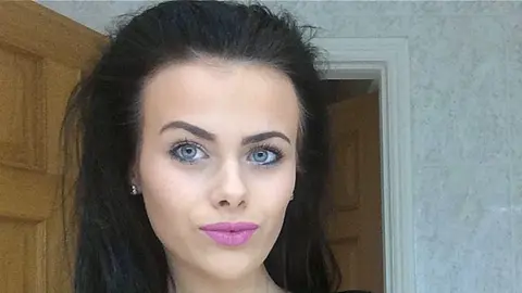 PA Media An image of India Chipchase, with long dark hair, standing in room with a door behind her. She has bright pink lipstick, painted eyebrows and has her black hair swept back.