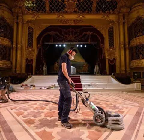 PA Media A man in a dust mask sanding the ballroom floor.