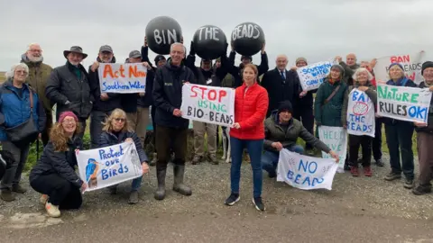 A group of people on a beach with banners opposing the use of biobeeds