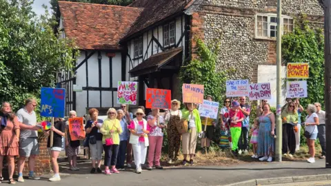 A group of campaigners standing in a line outside of Heath Barn holding signs and placards.