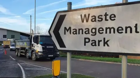 Dawid Wojtowicz/BBC Sign outside Waterbeach waste facility which says "Waste Management Park". There are waste trucks entering and leaving.