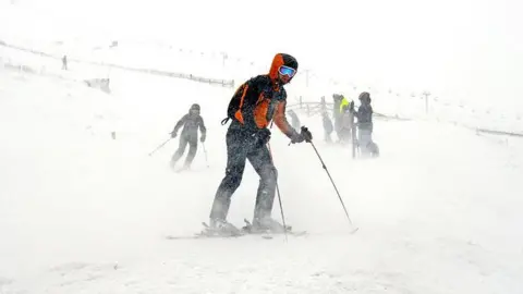 A skier wearing blue googles and black and orange clothing skis in front of other skiers.