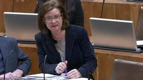 Senedd Cymru Eluned Morgan replying to one of Darren Millar's questions in the Senedd, surrounded by the wooden desks and computer laptops in the debating chamber 