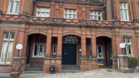 The exterior of Ipswich Museum. It is a large red building with the name of the museum above its entrance.