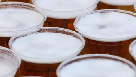 Clear plastic cups of amber beer with white foam.