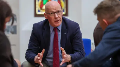 PA Media John Swinney sitting talking to two people while on a visit to the Hamilton constituency