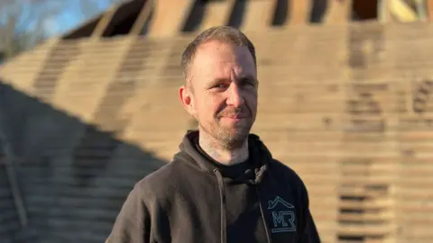 Builder standing on a partially tiled roof. 