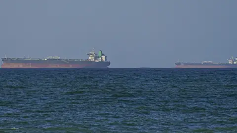Two cargo ships upon the horizon, water in the foreground.