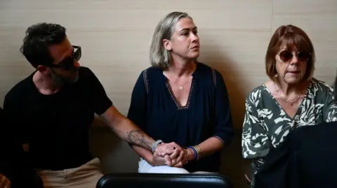 CHRISTOPHE SIMON/AFP Gisele Pelicot (R) sits beside her daughter Caroline Darian (C) and her son (L) at the courthouse during the trial of her husband accused of drugging her for nearly 10 years and inviting strangers to rape her at their home in Mazan, a small town in the south of France, in Avignon, on September 2, 2024