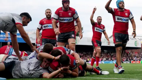 PA Media Gloucester's Freddie Thomas scores a try against Saracens at Kingsholm. He is underneath a pile of bodies while other Gloucester players celebrate in the background