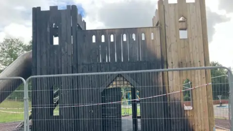 Robbie Kalus/BBC Wooden play equipment behind fence