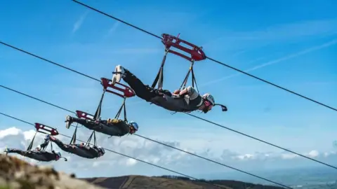 Four people hang from four separate zip lines in sunny Bethesda