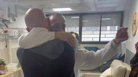 Family photo Eli Sharabi and Steve Brisley hugging in a hospital in Israel. 