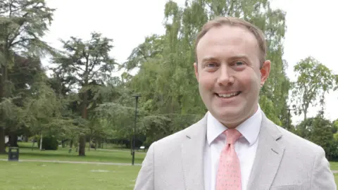 Kian Boyle/BBC A picture of Conservative MP Blake Stephenson, who is stood in a park. He is wearing a light grey suit jacket and a pink tie and white shirt.
