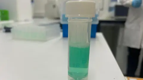 A sample pot with a green mouth rinse sample inside 