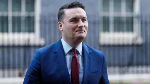 Getty Images Health Secretary Wes Streeting wearing a blue suit and red tie leaves Downing Street on 2 December 2025.