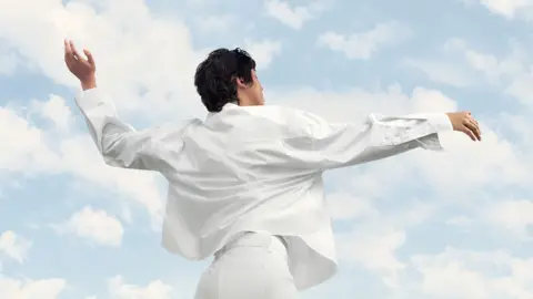 Person wearing all white in front of a backdrop of sky and clouds