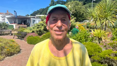 A man wearing a yellow t-shirt and a blue baseball cap, standing in a garden