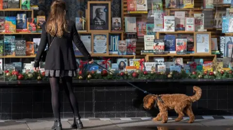 Getty Images A woman in black coat walking a brown dog outside a bookshop with Christmas decorations in window