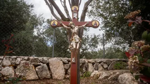 Israel Defense Forces A statue of Jesus on a cross erected in front of a fence atop a low stone wall