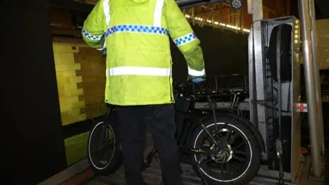 A Met Police officer places an e-bike onto a vehicle. 
