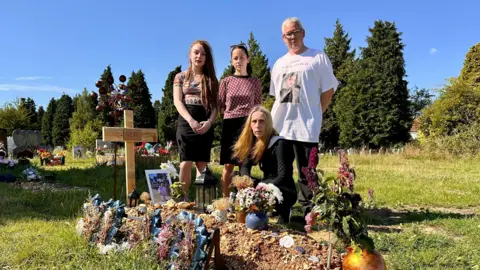 Vlad's family, Mia, Masha, Anna and Graham at Vald's graveside in Southampton which is covered in tributes and marked by a homemade wooden cross with his name on it