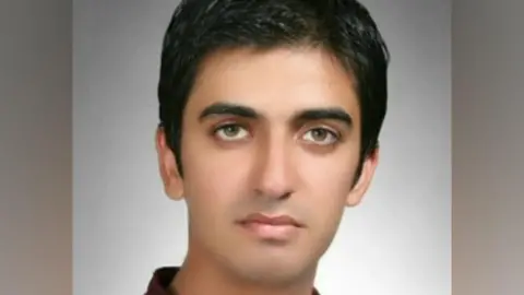 A profile-style image of Dr Jawad Ahmad - a man with shot black hair and wearing a dark shirt. He is standing in front of a grey background.