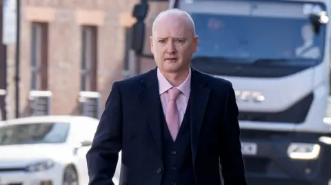 Graeme Dott arriving at the High Court in Glasgow. He is wearing a dark suit over a pink shirt witha pink tie.