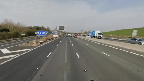 The M1 motorway with a slip road off to the left and a blue sign saying A509. There is not much traffic on the road.